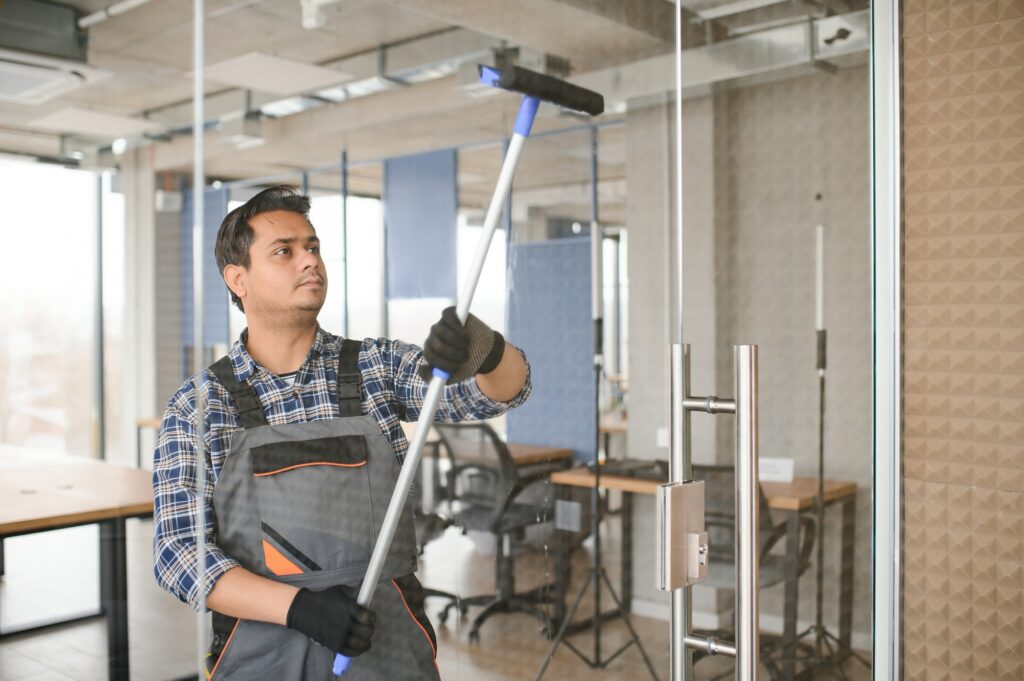 Male janitor cleaning window in office