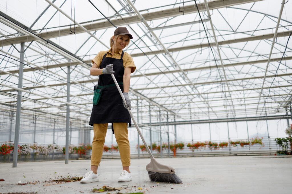 Woman in uniform sweeping in the greenhouse